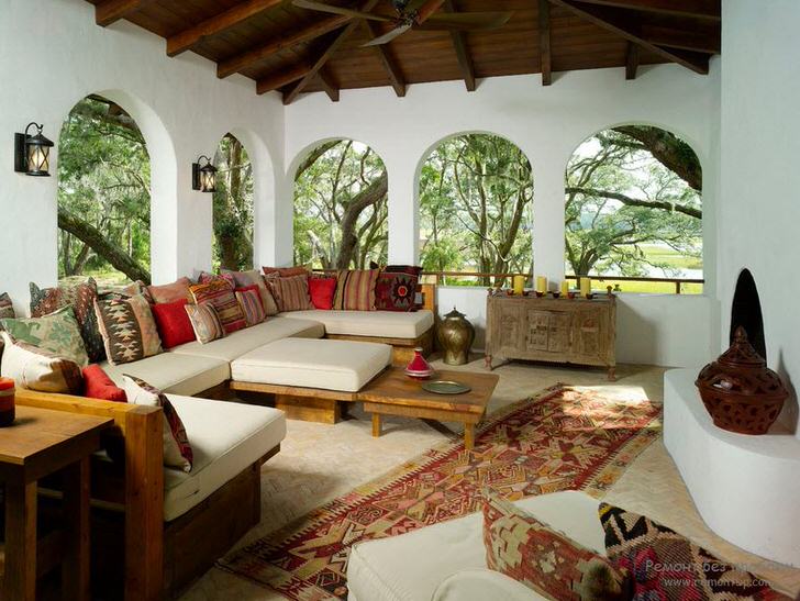 Веранда загородного дома оформлена в соответствии со средиземноморским стилем. Интересной особенностью становится декор большим количеством разноцветных подушек. 